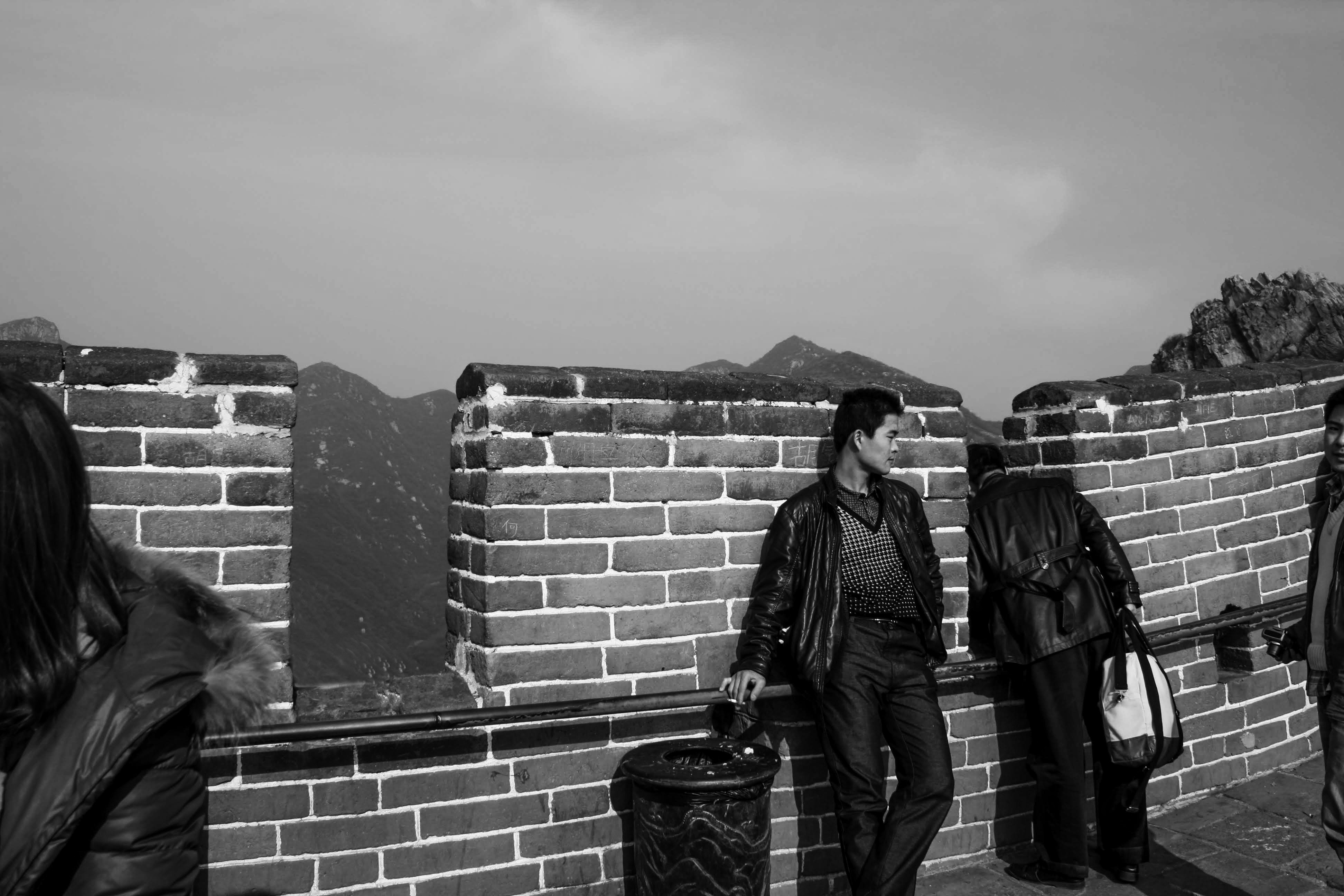 grayscale photography of man standing beside brick wall