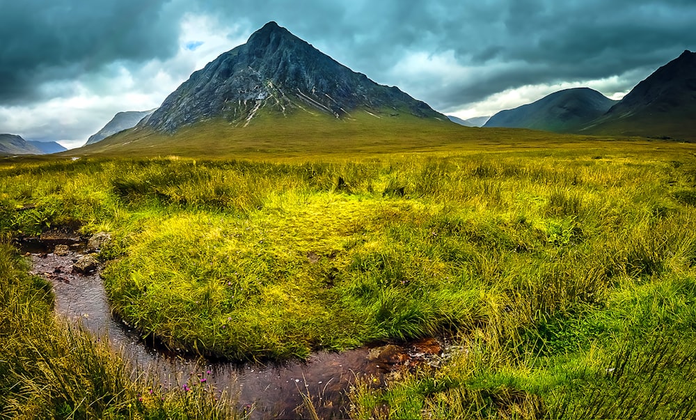 mountains and grass field under cloudy sky