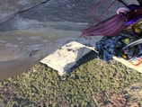 A climber is suspended on a vertical rock face, with various climbing gear such as ropes and carabiners visible in the foreground. Below is a vast view of a forested landscape, providing a dramatic perspective of height and exposure.