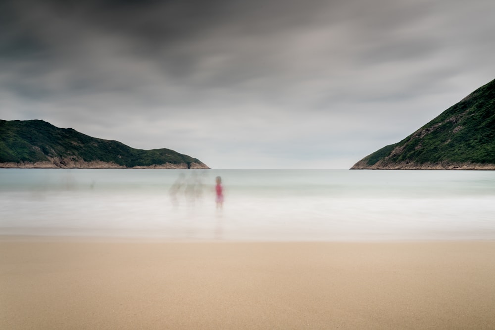 toddler standing on seashore near mountain range