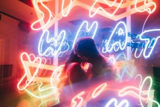 A couple is embracing in front of a vibrant background filled with colorful neon lights and signs, creating a lively and romantic atmosphere.
