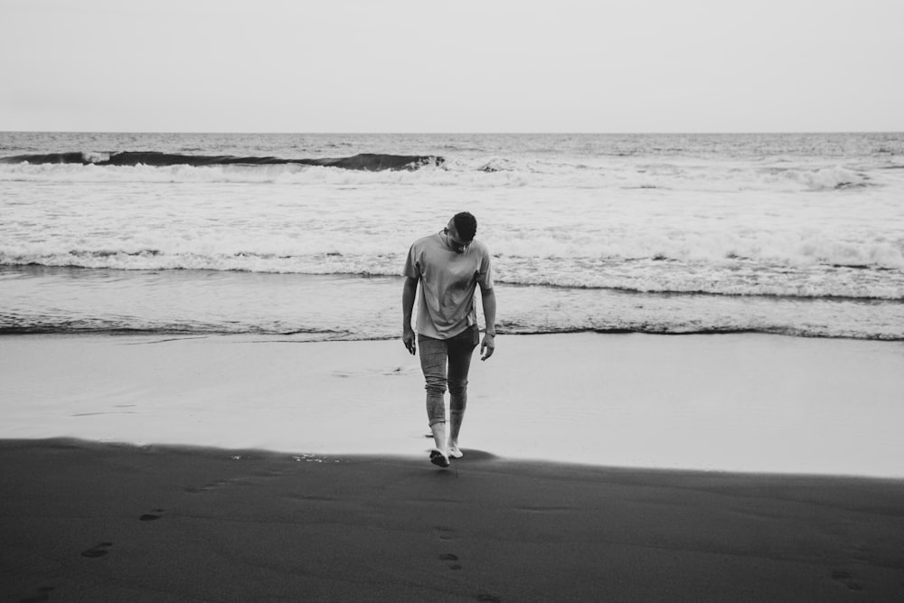 Graustufenfotografie eines Mannes, der am Meeresufer spazieren geht