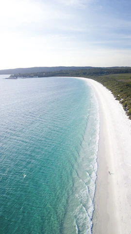A serene beach with crystal-clear waters and a luxury resort in the distance.
