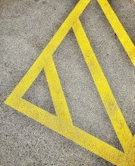 A textured asphalt surface marked with bright yellow diagonal lines forming a triangular pattern, often used for road or parking lot markings.