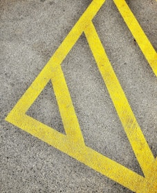 A textured asphalt surface marked with bright yellow diagonal lines forming a triangular pattern, often used for road or parking lot markings.