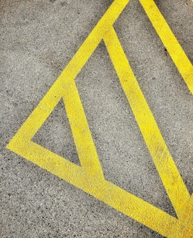 A textured asphalt surface marked with bright yellow diagonal lines forming a triangular pattern, often used for road or parking lot markings.
