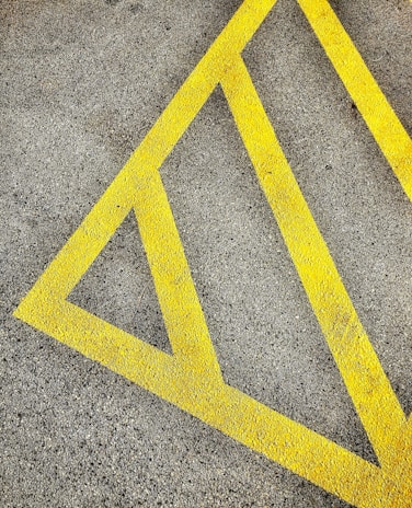 A textured asphalt surface marked with bright yellow diagonal lines forming a triangular pattern, often used for road or parking lot markings.