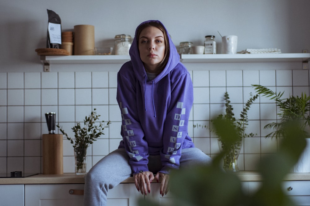 woman in purple pullover hoodie sitting on countertop