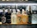 A selection of various bottled beverages are arranged on a refrigerated shelf. The lineup includes multiple types of Asian beers and sake, along with bottles of water. Each bottle displays unique and colorful labels featuring distinct branding and design elements.