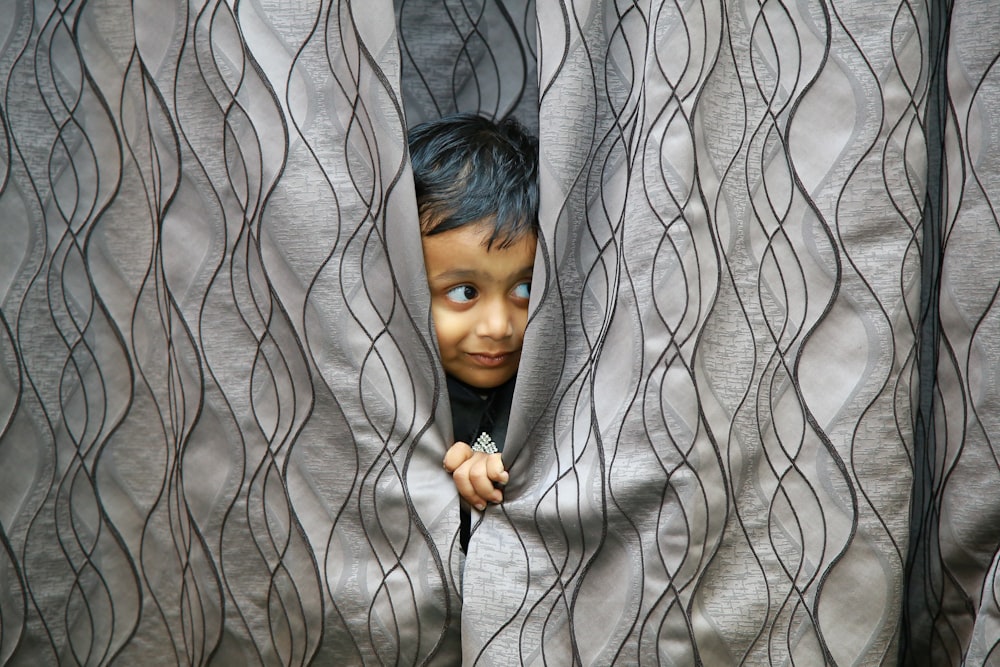 boy hiding behind of gray textile