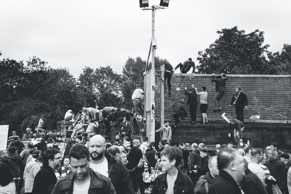 grayscale photography of people climbing on fence