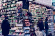 A bustling market stall is filled with a wide array of mobile phone cases and accessories, displayed on shelves and racks. Several people are browsing the items, dressed warmly for the weather. The cases come in various colors and designs, adding vibrancy to the scene.