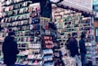 A bustling market stall is filled with a wide array of mobile phone cases and accessories, displayed on shelves and racks. Several people are browsing the items, dressed warmly for the weather. The cases come in various colors and designs, adding vibrancy to the scene.