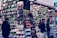 A bustling market stall is filled with a wide array of mobile phone cases and accessories, displayed on shelves and racks. Several people are browsing the items, dressed warmly for the weather. The cases come in various colors and designs, adding vibrancy to the scene.