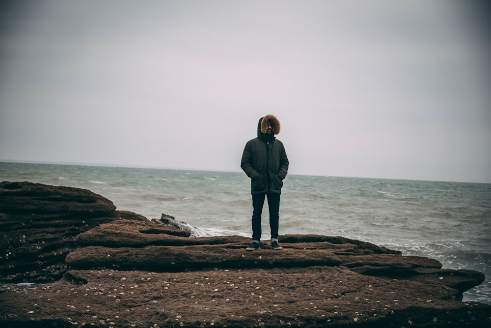 homme en parka debout au bord de la mer