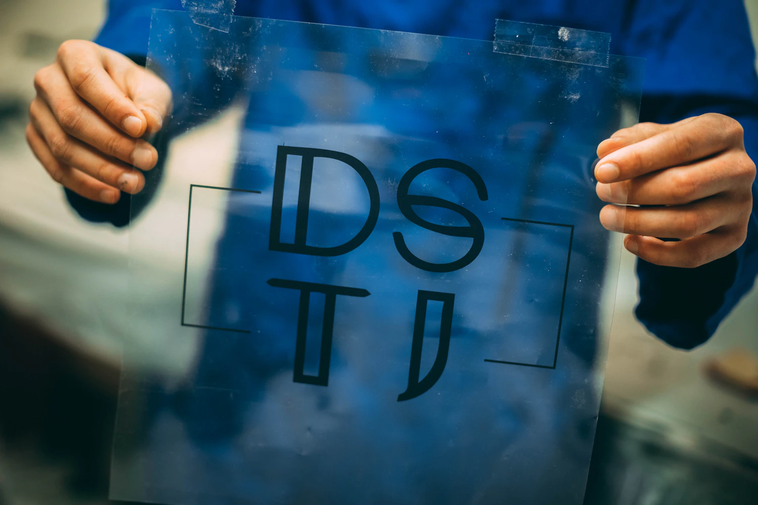 Hands holding up an exposed screen-printing screen with lettering in the stencil