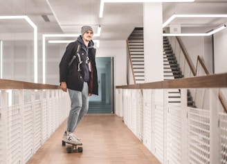 A beginner learning to balance on a smooth wooden skateboard indoors.