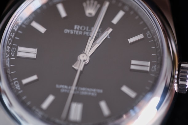 Close-up view of a luxury wristwatch featuring a sleek black dial with silver hour markers and hands, encased in a polished stainless steel. The branding and model information are visible on the dial, emphasizing elegance and precision.
