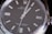 Close-up view of a luxury wristwatch featuring a sleek black dial with silver hour markers and hands, encased in a polished stainless steel. The branding and model information are visible on the dial, emphasizing elegance and precision.