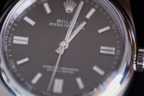 Close-up view of a luxury wristwatch featuring a sleek black dial with silver hour markers and hands, encased in a polished stainless steel. The branding and model information are visible on the dial, emphasizing elegance and precision.