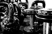 Kettlebells and dumbbells arranged on a gym floor. The equipment appears worn, indicating frequent use. The setting suggests a focus on strength training.