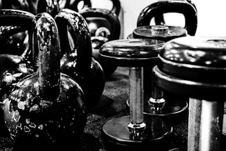 Kettlebells and dumbbells arranged on a gym floor. The equipment appears worn, indicating frequent use. The setting suggests a focus on strength training.