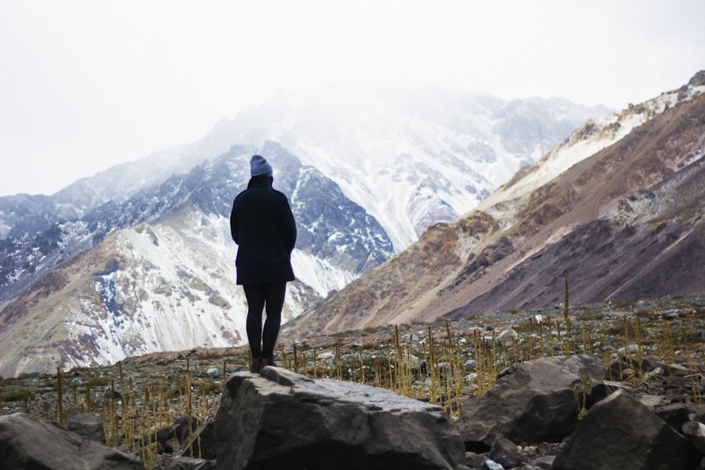 man standing near rock facing mountains