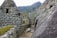 Stone structures featuring ancient, Incan architectural design with terraced hillsides in the background. The setting is mountainous and lush with greenery.