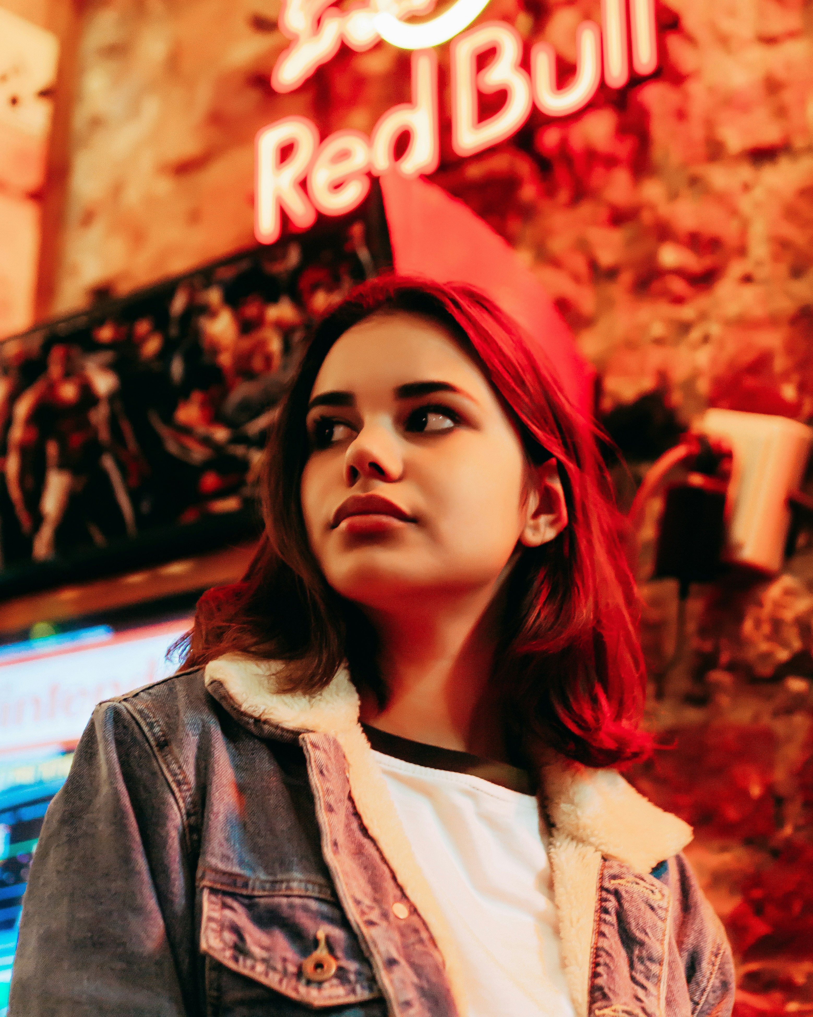Woman wearing blue denim jacket standing near the Red Bull neon light