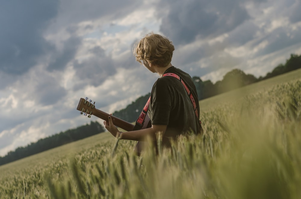 man paying guitar in the middle of green field during daytime