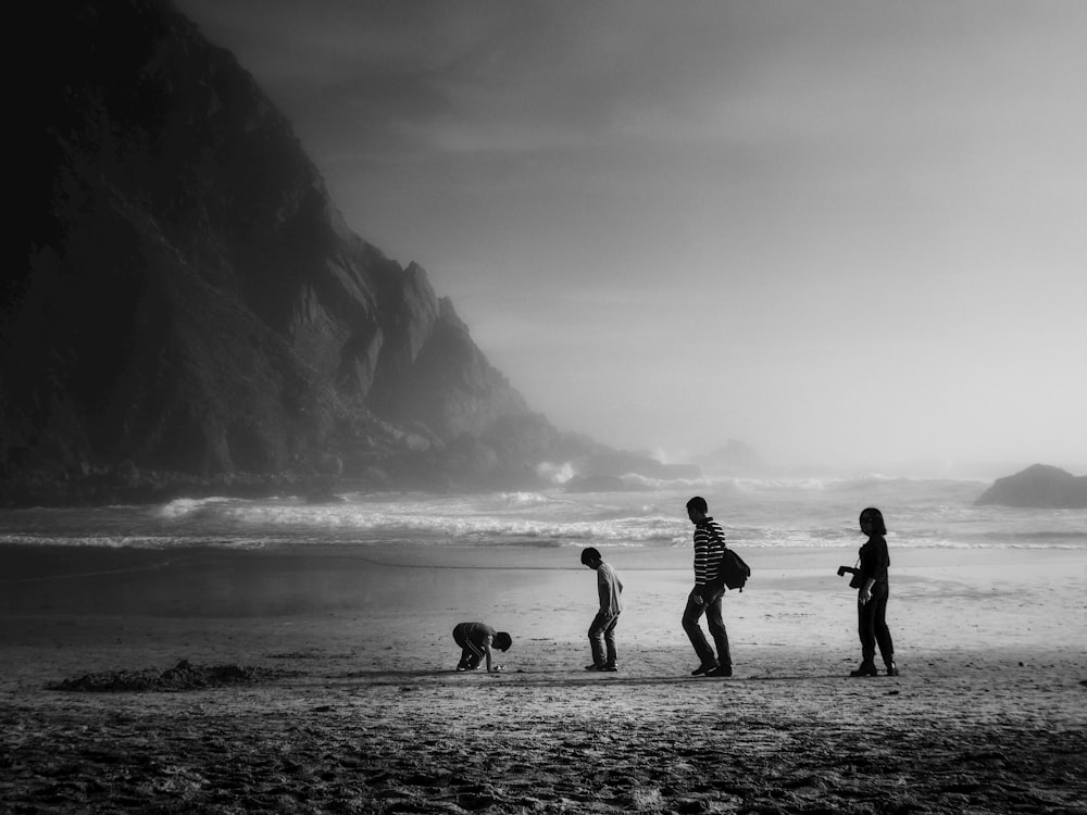grayscale photo of four person standing at the beach