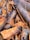 A close-up view of cinnamon bark pieces, displaying textured surfaces and various shades of brown and gray. The pieces are irregularly shaped and densely packed, highlighting the natural, rugged texture.