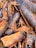 A close-up view of cinnamon bark pieces, displaying textured surfaces and various shades of brown and gray. The pieces are irregularly shaped and densely packed, highlighting the natural, rugged texture.