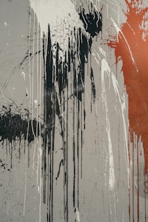 Abstract art featuring long vertical drips of black, white, and red paint on a gray canvas. The paint appears to be splashed and spattered with areas of cracking, suggesting movement and intensity.