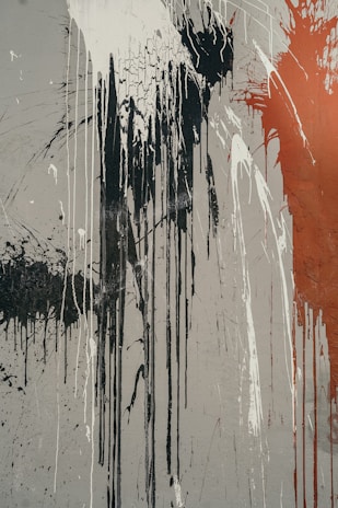 Abstract art featuring long vertical drips of black, white, and red paint on a gray canvas. The paint appears to be splashed and spattered with areas of cracking, suggesting movement and intensity.