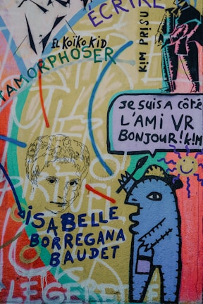Colorful graffiti art featuring a mix of abstract and recognizable elements, including a stylized humanoid figure, sketches of faces, and various texts in different fonts and colors spread throughout. The artwork is vibrant with a mix of flowing lines and sharp outlines, incorporating a mix of languages and styles.