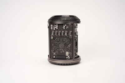 A cylindrical computer component with visible internal circuitry and components. The casing is open to reveal intricate electronic parts, including chips, capacitors, and other hardware elements. The component is placed against a plain, light background.