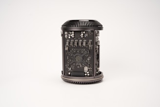 A cylindrical computer component with visible internal circuitry and components. The casing is open to reveal intricate electronic parts, including chips, capacitors, and other hardware elements. The component is placed against a plain, light background.