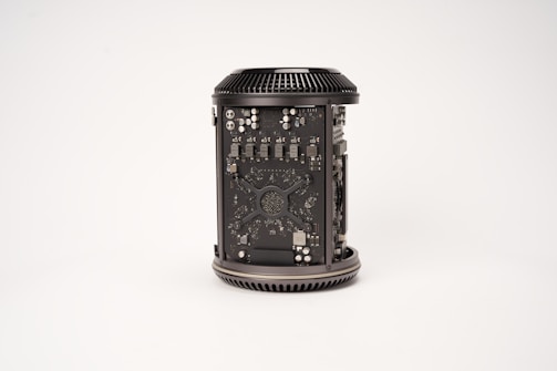 A cylindrical computer component with visible internal circuitry and components. The casing is open to reveal intricate electronic parts, including chips, capacitors, and other hardware elements. The component is placed against a plain, light background.