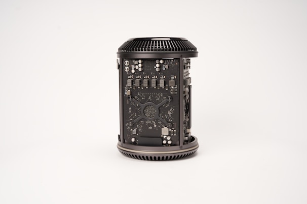 A cylindrical computer component with visible internal circuitry and components. The casing is open to reveal intricate electronic parts, including chips, capacitors, and other hardware elements. The component is placed against a plain, light background.