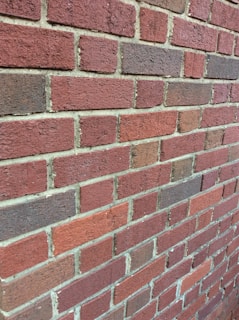 A close-up view of a red brick wall with visible mortar lines in between each brick. The bricks have varying shades of red and brown, creating a textured appearance.