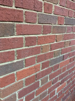 A close-up view of a red brick wall with visible mortar lines in between each brick. The bricks have varying shades of red and brown, creating a textured appearance.