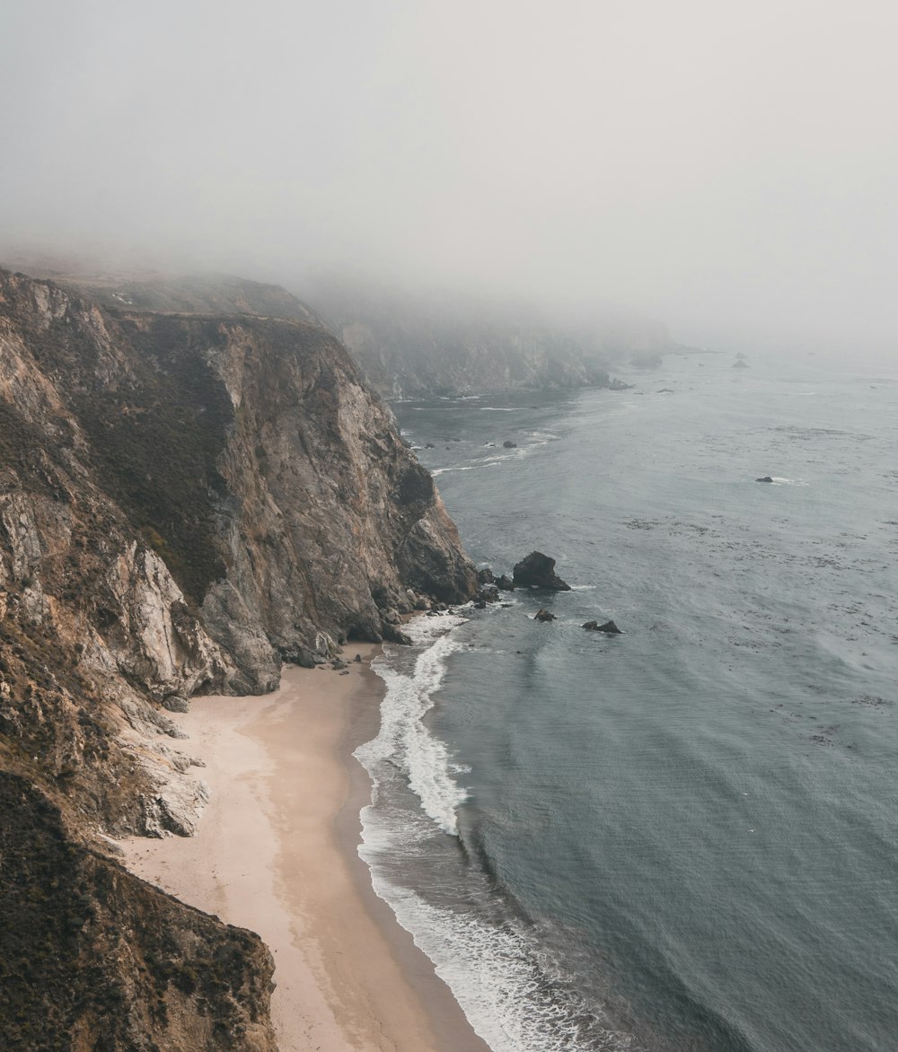 water hitting rocks on shore near cliff during daytime