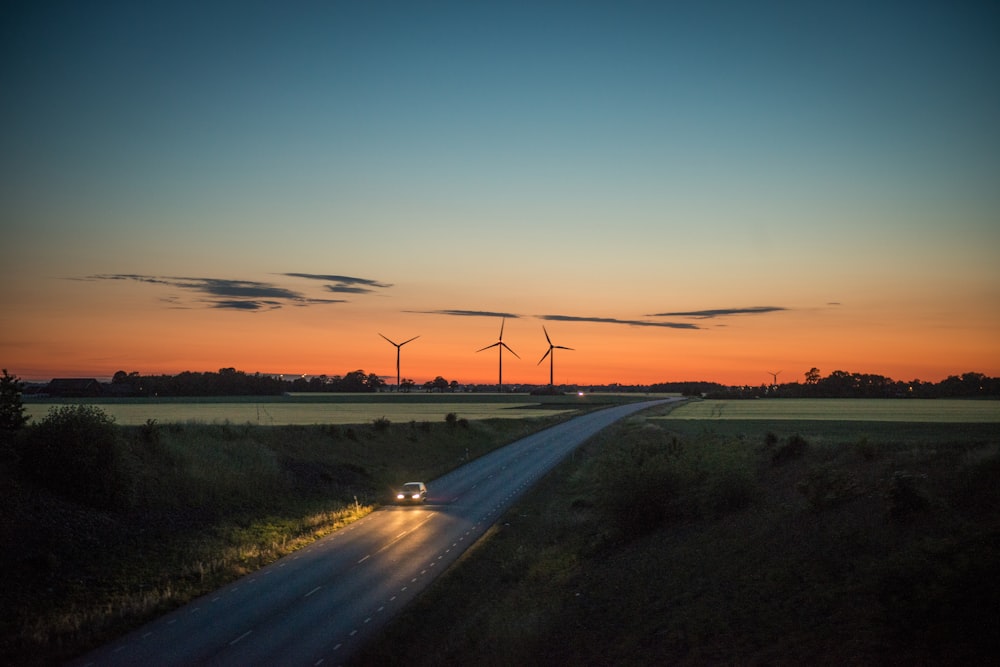 car passing by on road with wind turbines from far behind