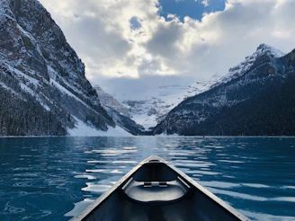 A tranquil lake reflecting snow-capped peaks with a lone canoe drifting quietly.