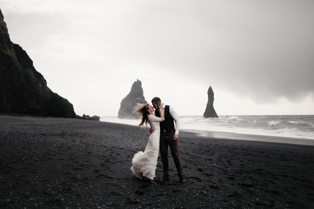 Photographie en niveaux de gris du marié et de la mariée s’embrassant sur la plage