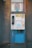 A vintage public payphone with a handset, keypad, and coin slot is mounted on an old, weathered metal panel. The surrounding metal surface shows signs of rust and graffiti marks, adding to the aged appearance.