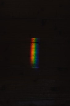 A spectrum of rainbow colors appears as a vertical band against a dark background. The colors transition smoothly from red to violet, creating a vivid contrast with the surrounding darkness.