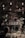 A dimly lit setting featuring a vintage chandelier with glowing candles hanging above a rustic table. Beneath it, a sign reads 'Wine Tasting' surrounded by lush floral arrangements, leaves, and decorative wine barrels. The ambiance suggests a cozy and elegant environment for a wine event.