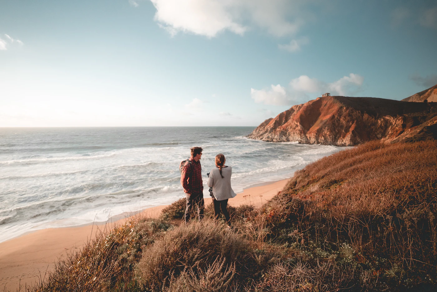 A couple on a grassy clifftop above the sea at sunset